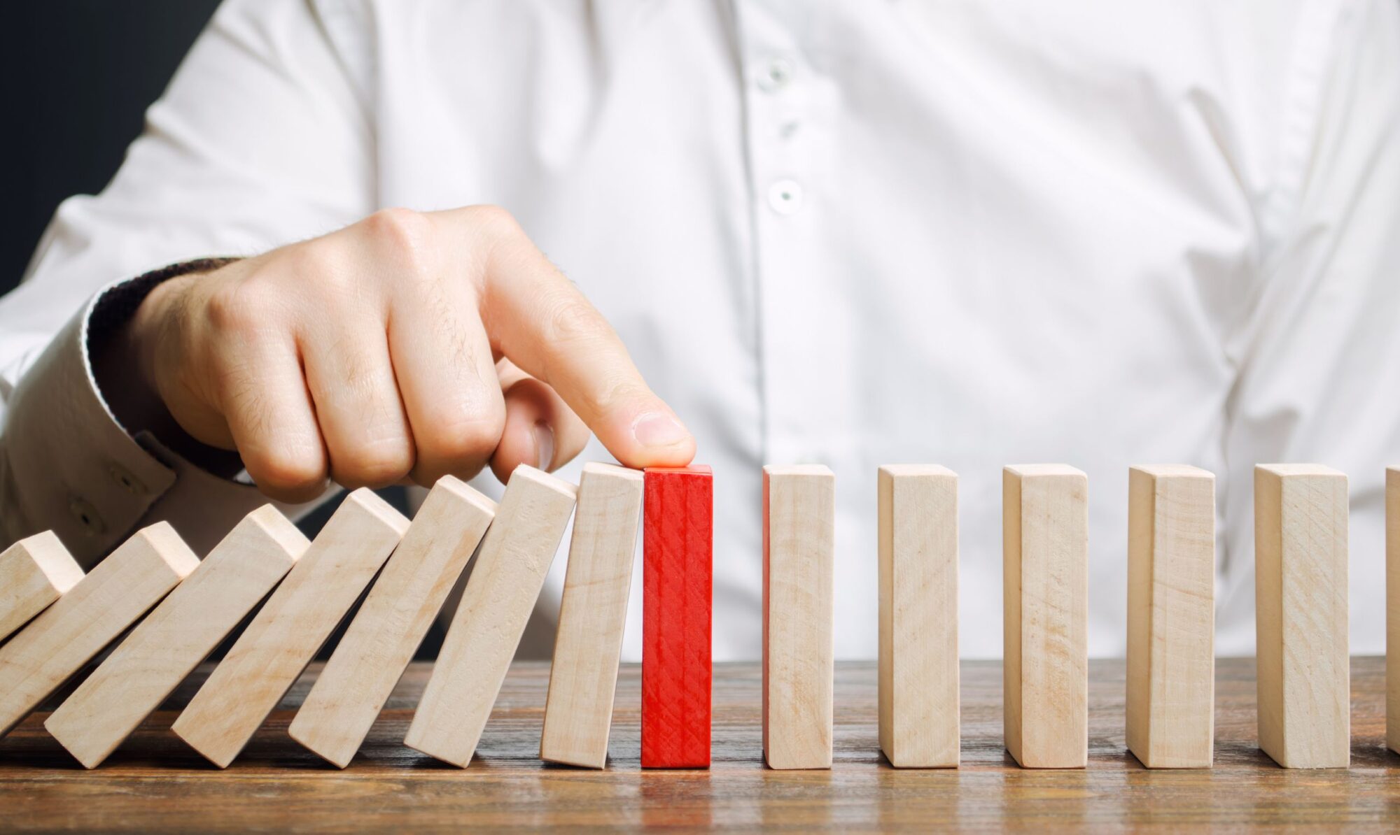 Closeup photo of the hand of a business person stopping the fall of domino-like blocks